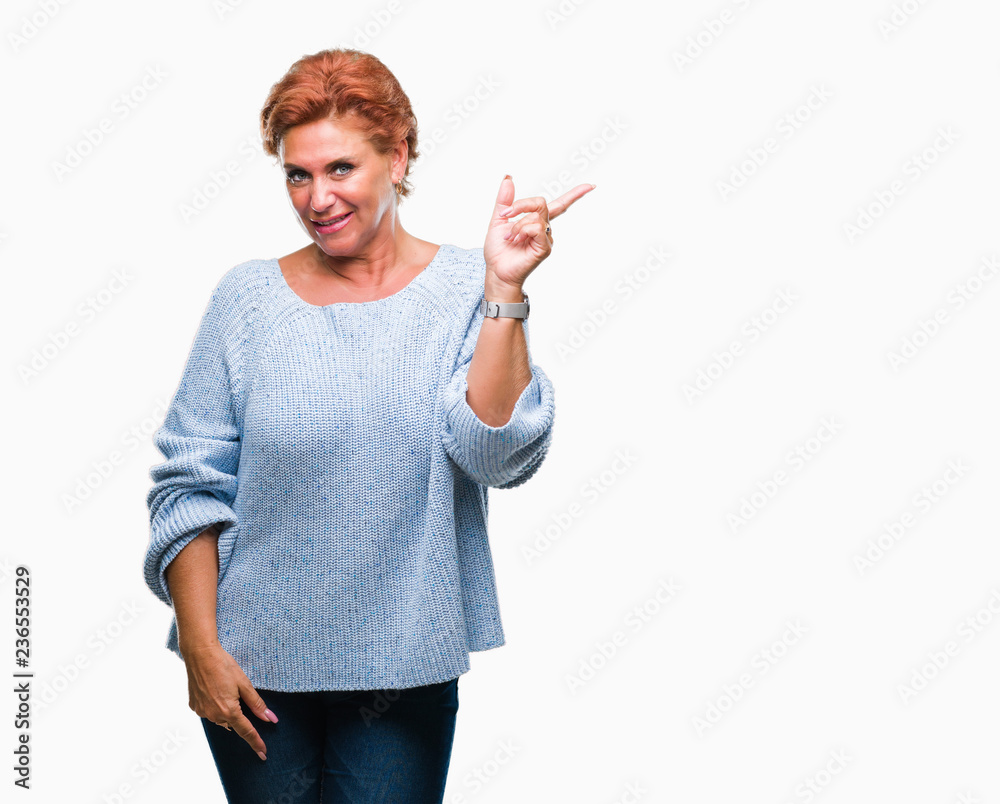 Atrractive senior caucasian redhead woman wearing winter sweater over isolated background with a big smile on face, pointing with hand and finger to the side looking at the camera. Atrractive senior caucasian redhead woman wearing winter sweater over isolated background with a big smile on face, pointing with hand and finger to the side looking at the camera.