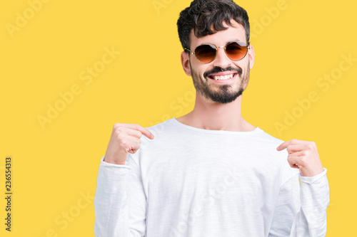 Young handsome man wearing sunglasses over isolated background looking confident with smile on face, pointing oneself with fingers proud and happy.