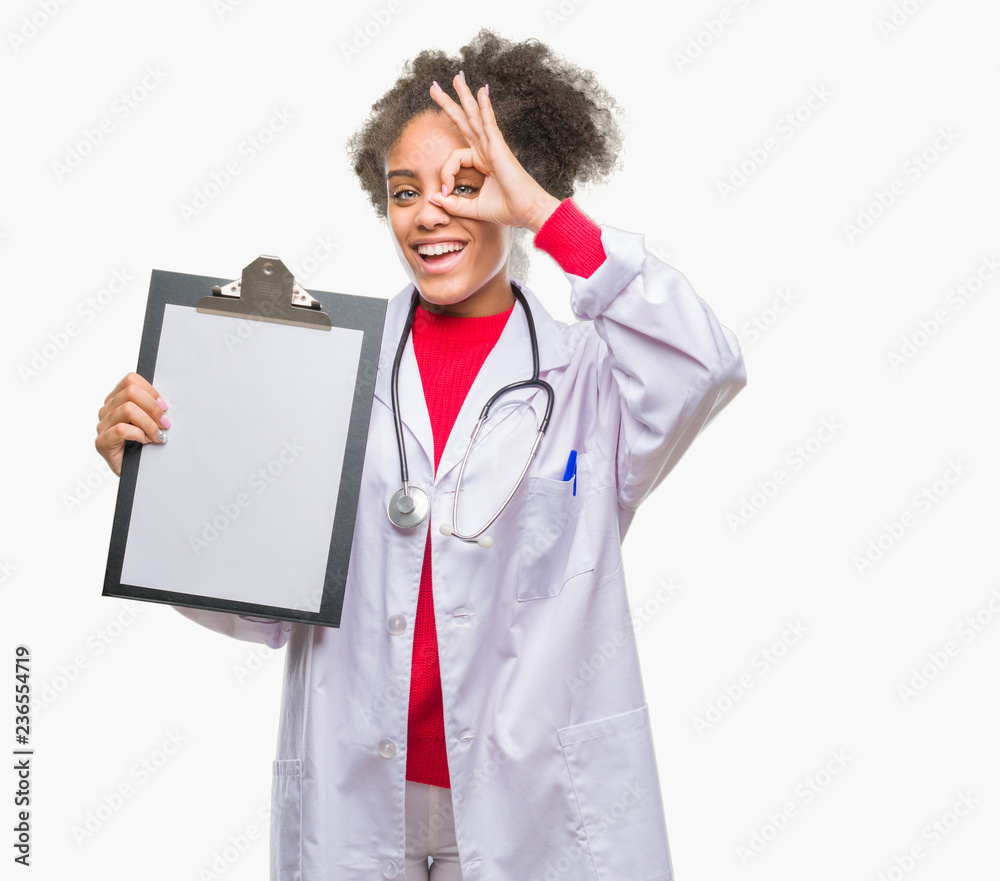 Young afro american doctor woman holding clipboard over isolated background with happy face smiling doing ok sign with hand on eye looking through fingers Young afro american doctor woman holding clipboard over isolated background with happy face smiling doing ok sign with hand on eye looking through fingers