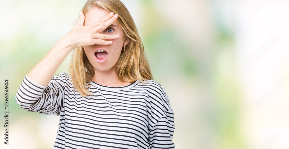 Beautiful young woman wearing stripes sweater over isolated background peeking in shock covering face and eyes with hand, looking through fingers with embarrassed expression. Beautiful young woman wearing stripes sweater over isolated background peeking in shock covering face and eyes with hand, looking through fingers with embarrassed expression.
