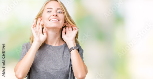 Beautiful young woman wearing oversize casual t-shirt over isolated background Trying to hear both hands on ear gesture, curious for gossip. Hearing problem, deaf © Krakenimages.com