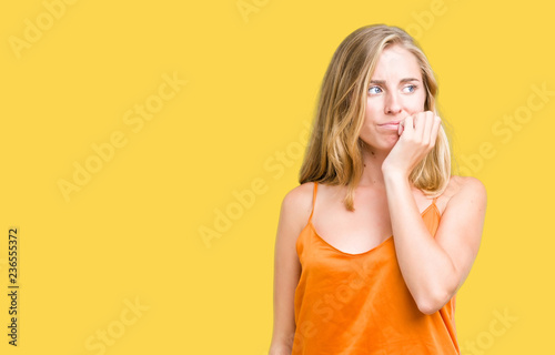 Beautiful young woman wearing orange shirt over isolated background looking stressed and nervous with hands on mouth biting nails. Anxiety problem.