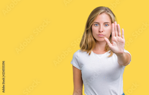 Beautiful young woman wearing casual white t-shirt over isolated background doing stop sing with palm of the hand. Warning expression with negative and serious gesture on the face.