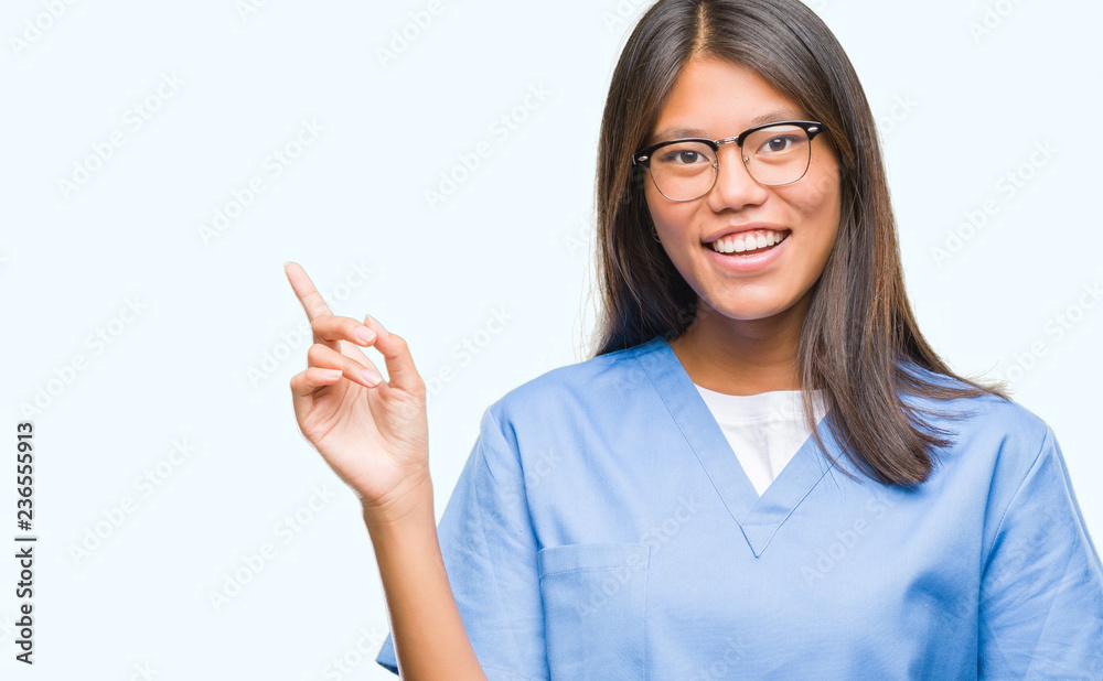Young asian doctor woman over isolated background with a big smile on face, pointing with hand and finger to the side looking at the camera. Young asian doctor woman over isolated background with a big smile on face, pointing with hand and finger to the side looking at the camera.