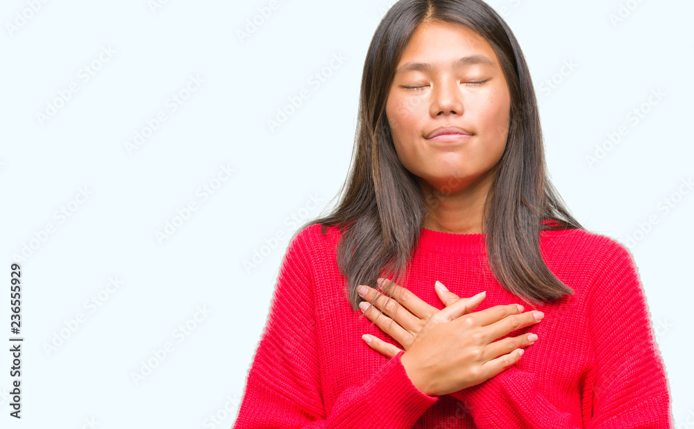 Young asian woman wearing winter sweater over isolated background smiling with hands on chest with closed eyes and grateful gesture on face. Health concept. Young asian woman wearing winter sweater over isolated background smiling with hands on chest with closed eyes and grateful gesture on face. Health concept.