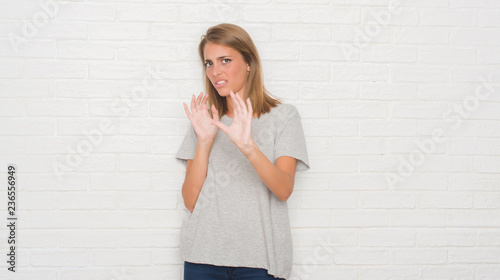 Beautiful young woman over white brick wall disgusted expression, displeased and fearful doing disgust face because aversion reaction. With hands raised. Annoying concept. © Krakenimages.com