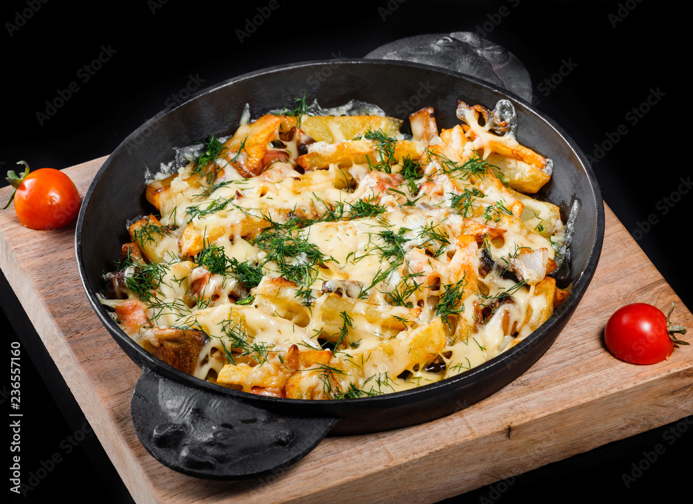 Roasted or baked potato in frying pan with tomatoes, herbs and cheese on wooden board, isolated on black background, homemade food. Top view Roasted or baked potato in frying pan with tomatoes, herbs and cheese on wooden board, isolated on black background, homemade food. Top view