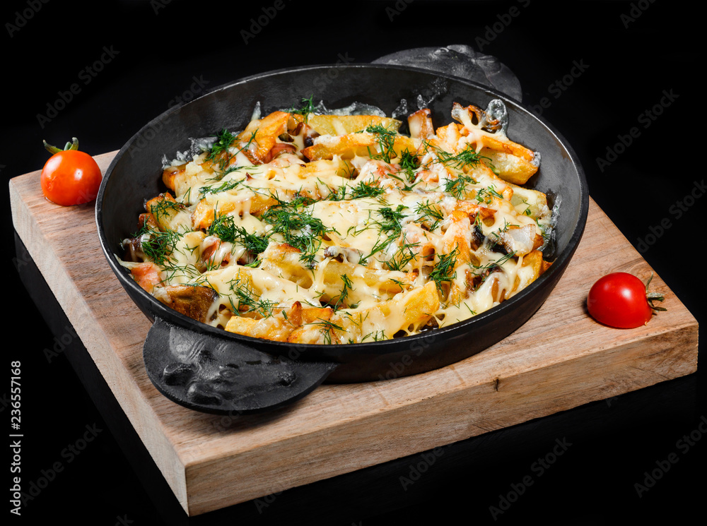 Roasted or baked potato in frying pan with tomatoes, herbs and cheese on wooden board, isolated on black background, homemade food. Top view Roasted or baked potato in frying pan with tomatoes, herbs and cheese on wooden board, isolated on black background, homemade food. Top view