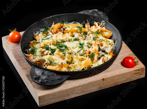 Roasted or baked potato in frying pan with tomatoes, herbs and cheese on wooden board, isolated on black background, homemade food. Top view