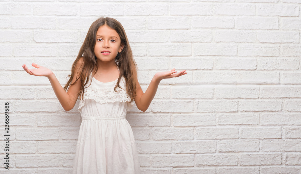 Young hispanic kid over white brick wall clueless and confused expression with arms and hands raised. Doubt concept. Young hispanic kid over white brick wall clueless and confused expression with arms and hands raised. Doubt concept.