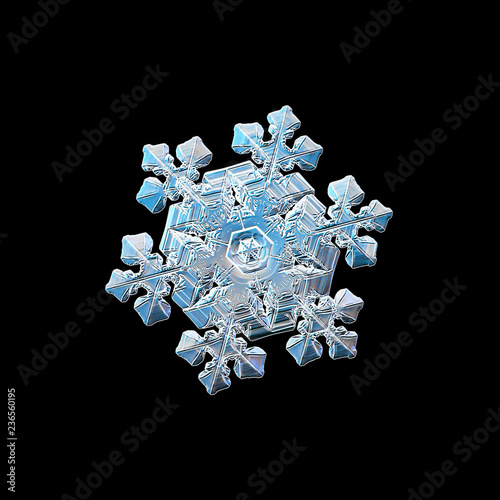 Snowflake isolated on black background. Macro photo of real snow crystal: elegant star plate with fine hexagonal symmetry, glossy relief surface, massive central hexagon and complex inner details.
