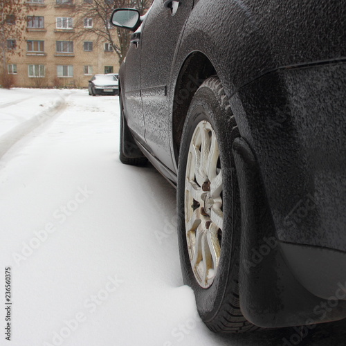 Down rear side view of the car and wheel on alloy disk, covered with ice crust in winter day - season driving, icy rain, icing vehicle after snowfall photo