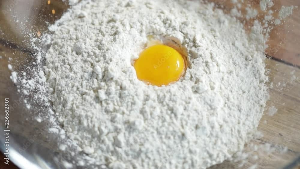 An Egg Yolk Falling into a Pile of Flour on a Wooden Table An Egg Yolk Falling into a Pile of Flour on a Wooden Table