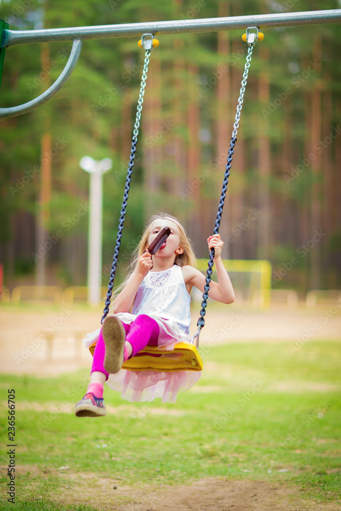 Little blonde girl smiling swinging outdoors on a playgroung Little blonde girl smiling swinging outdoors on a playgroung