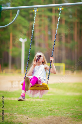 Little blonde girl smiling swinging outdoors on a playgroung