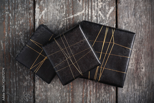 Three gifts wrapped in black with golden string on wooden surfac photo