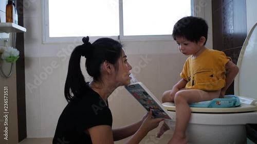 mother reading book with her son sitting on flush toilet