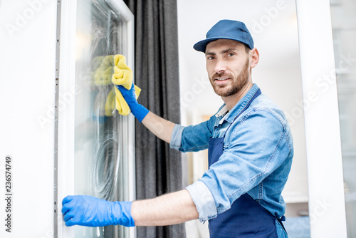 Cuadro en lienzo Man as a professional cleaner in blue uniform washing window with cotton wiper i