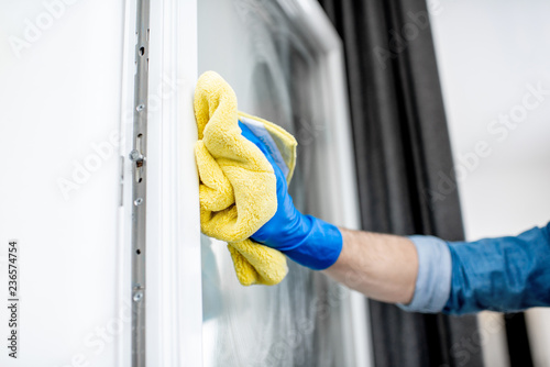 Close-up of a man in protective glove washing window glass with yellow cotton wiper