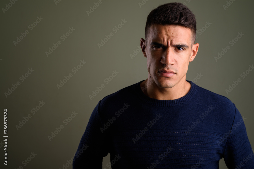 Young angry man wearing sweater against colored background