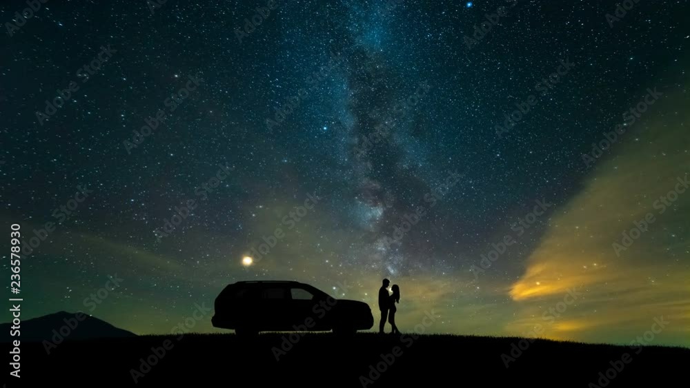 The man and woman standing near a car against the starry sky. time lapse