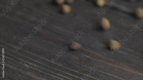Pimento or Allspice grains are rolling down on a wooden board from the left side to the right, Closeup