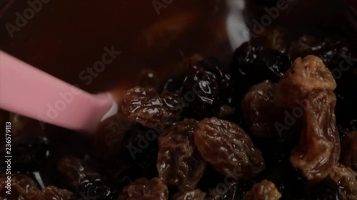 Raisins in a Dark Liquid become Stirred with a Pink Spoon (hand not visible), Closeup