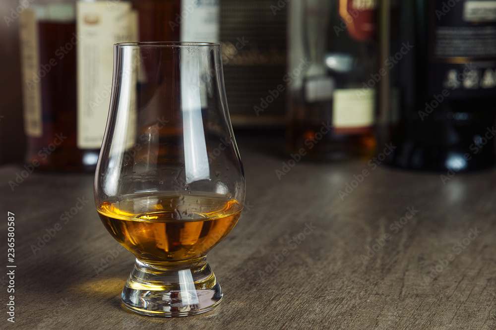 Whisky glass with single malt scotch on wooden table and scotch bottles on the background Whisky glass with single malt scotch on wooden table and scotch bottles on the background