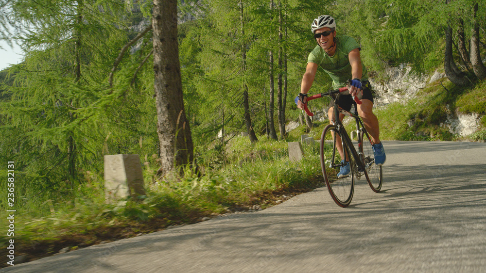 LOW ANGLE: Cheerful male road cyclist enjoying a scenic ride through the forest.