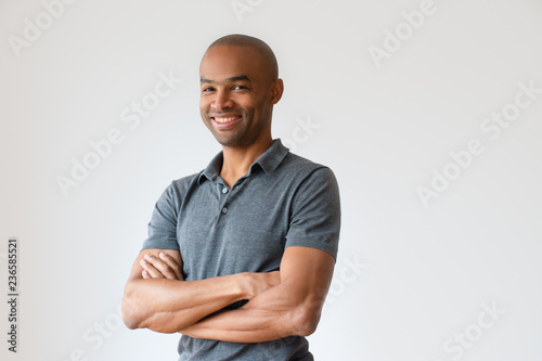 Happy successful African American man with toothy smile. Confident smiling man posing in gray T-shirt with crossed arms. Success concept