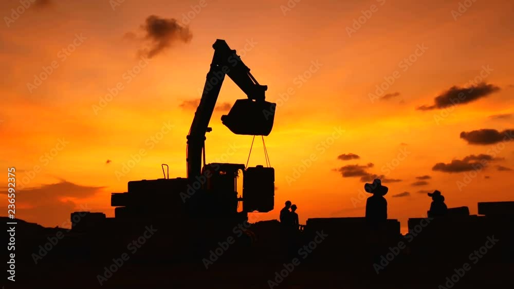 Construction Video At construction site The silhouette excavator is digging ground and lifting a large mortar, with engineering and construction workers to help with colorful sunset .