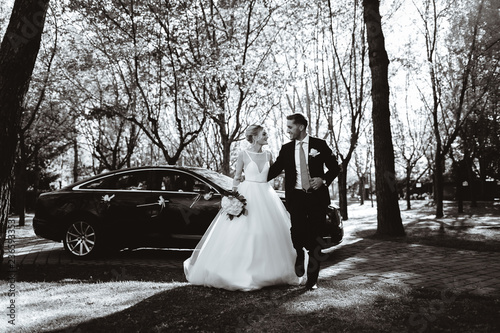 Bride and groom take photos near a black car. Black and white picture.