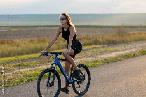 A girl riding a mountain bike on an asphalt road, beautiful portrait of a cyclist at sunset