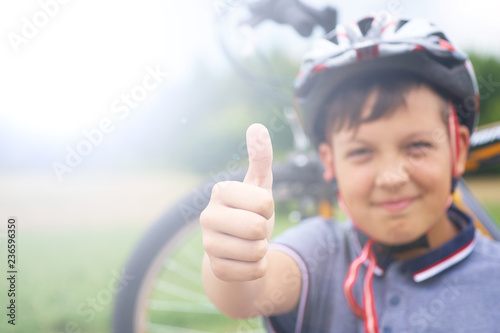 Riding is super. Portrait of smiling teenager riding bike and giving thumbs up on background of park and bike.