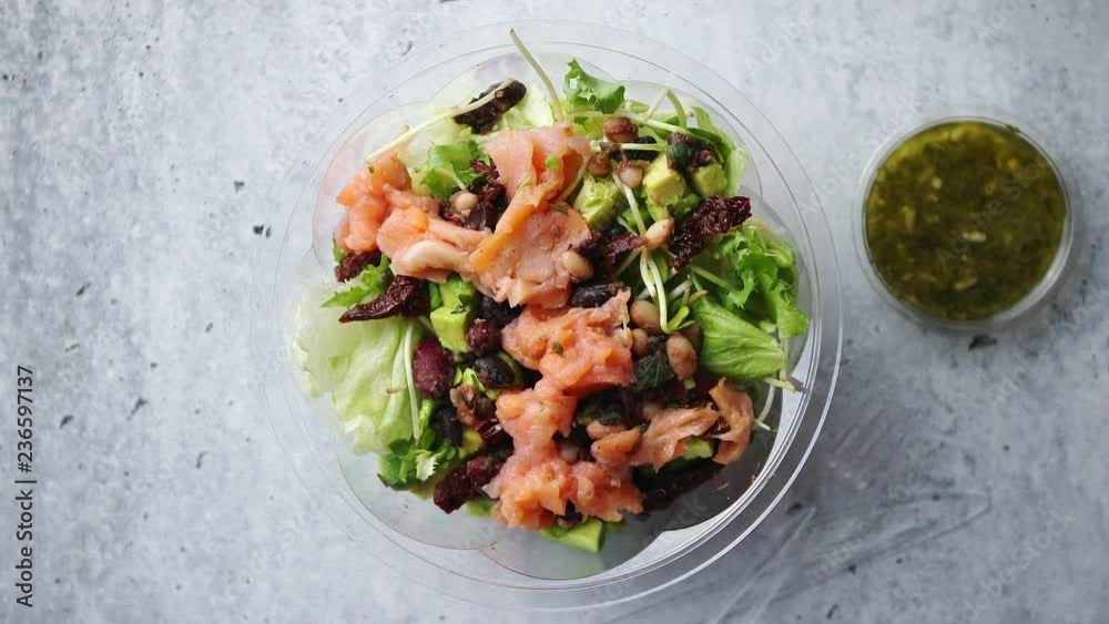A delicious smoked salmon take away salad with smoked salmon, lettuce, mixed baby greens, beans, dry tomatoes, cherry tomatoes and red onion with green sauce.