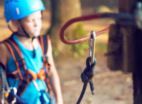 Cute little boy in blue shirt and helmet having fun at the adventure park, holding ropes and prepering to climb wooden stairs. Hobby, active lifestyle concept.