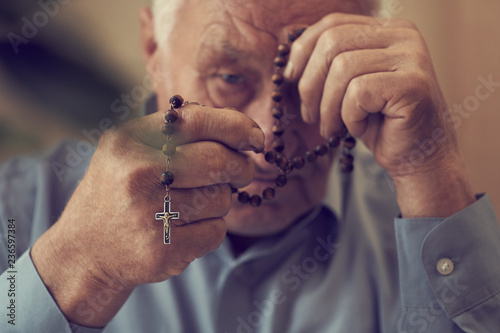 Praying hands of an old man holding rosary beads.