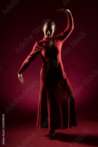 Lady in red gown standing and posing  in studio. Portrait of beautiful elegant woman in evening dress
