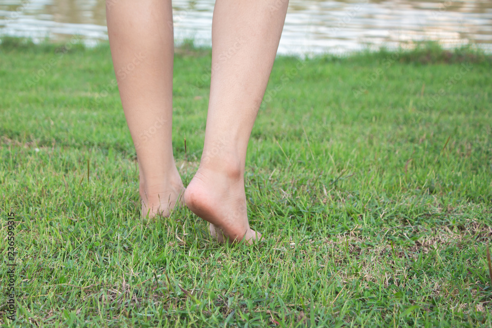 Woman legs walking on green grass near river.