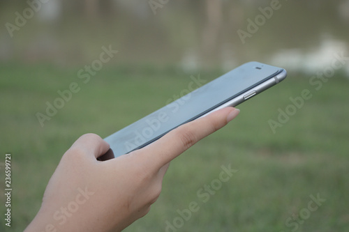 woman hand hold and touch screen smart phone or cellphone on blurred green background.