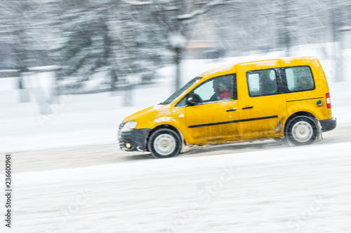 Driving in snow. Motion in blur yellow car in heavy snowfall in city road. Abstract blur winter weather background