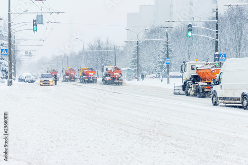 Snow plow trucks column removes snow from the city road. Snowstorm in the city - seasonal abstract motion blur background