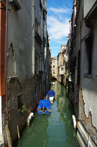 Three covered boats in a narrow Venetian canal. Houses with old plaster