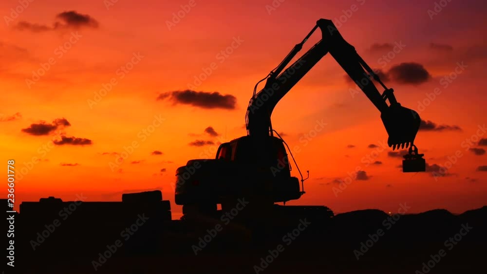 Construction Video At construction site The silhouette excavator is digging ground and lifting a large mortar, with engineering and construction workers to help with colorful sunset .