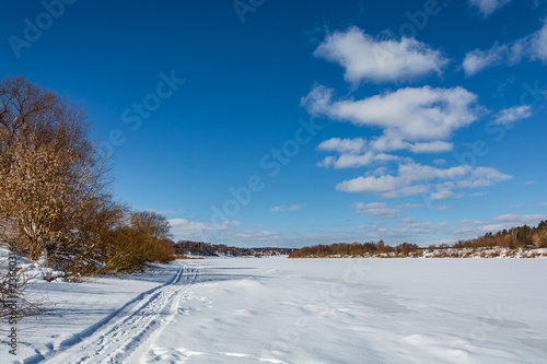 winter landscape with frozen river, trees and a city in the distance 