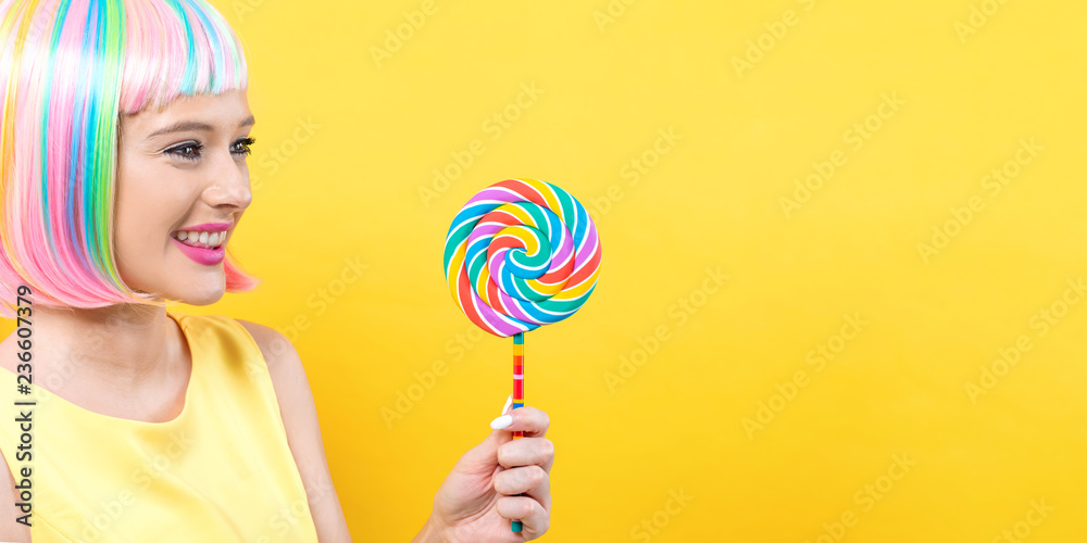 Woman in a colorful wig with a giant lollipop on a yellow background