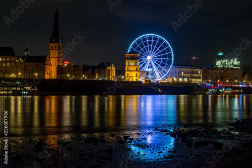Photography Night scenery colorful illuminated and reflected on river of buildings in old town, big moving Ferris Wheel and  Christmas Market on promenade along riverside Rhine River in Düsseldorf, Germany
