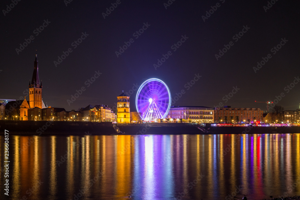 Night scenery colorful illuminated and reflected on river of buildings in old town, big moving Ferris Wheel and  Christmas Market on promenade along riverside Rhine River in Düsseldorf, Germany. 