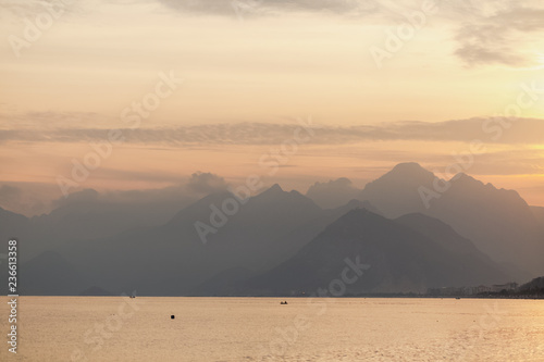 Beautiful skyscape with calm sea water and mountains seen far away in distance during sunset time. Antalya city, Turkey, Mediterranean sea. Horizontal color photography.