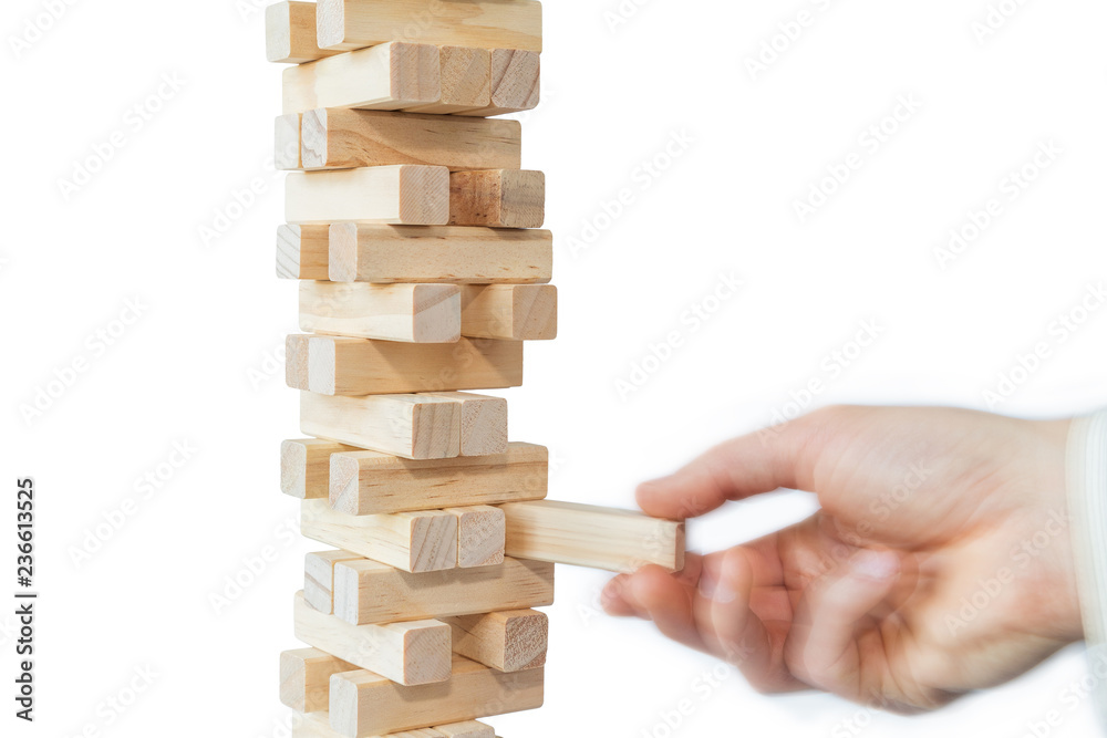 Man's hand taking or putting a block to an unstable and incomplete tower of wooden blocks. Concept photo of planning, taking risks and strategizing. Hand is in motion. Isolated on white background. Man's hand taking or putting a block to an unstable and incomplete tower of wooden blocks. Concept photo of planning, taking risks and strategizing. Hand is in motion. Isolated on white background.